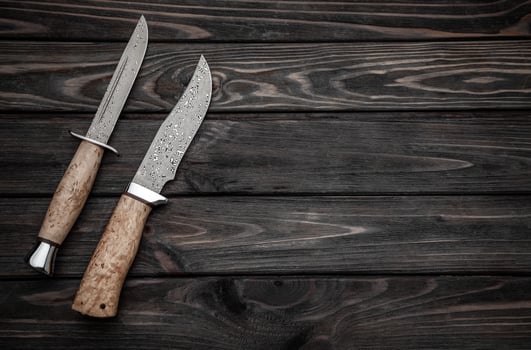 Hunting bowie knife with a wooden handle on dark wooden background. Steel arms weapon. top view photo