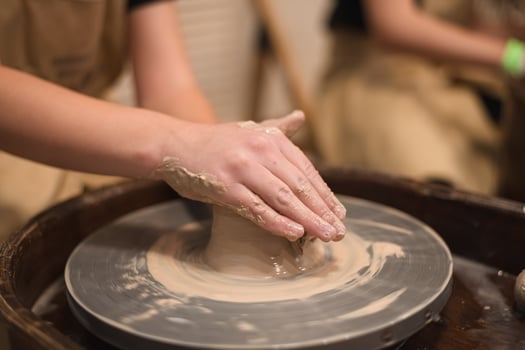 Potter girl works on potter's wheel, making ceramic pot out of clay in pottery workshop photo