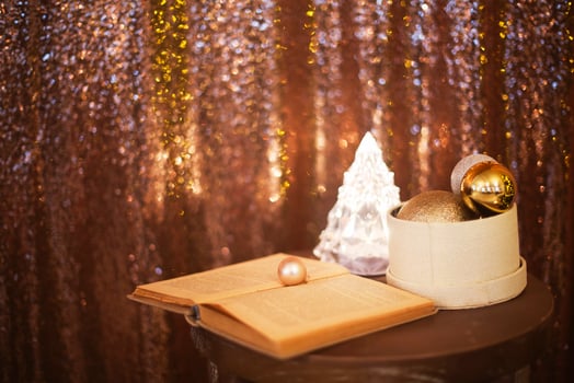 Little box with a lot of Christmas silver and golden decorations near the Christmas tree lamp and the book photo