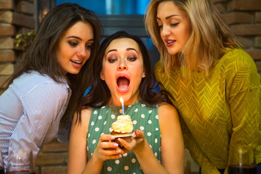 Portrait of joyful young woman holding birthday cupcake surrounded by friends photo