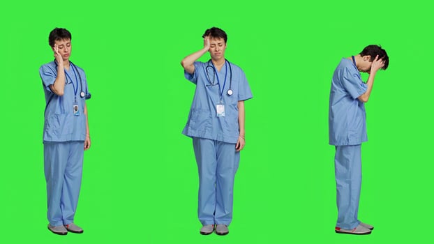 Unwell nurse suffering from a headache against greenscreen backdrop, wearing scrubs and feeling overworked at hospital. Medical assistant having a painful migraine, stress and burnout. Camera A. photo