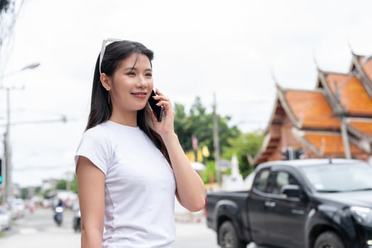 A beautiful Asian woman is talking on the phone while standing by the street in the city. photo