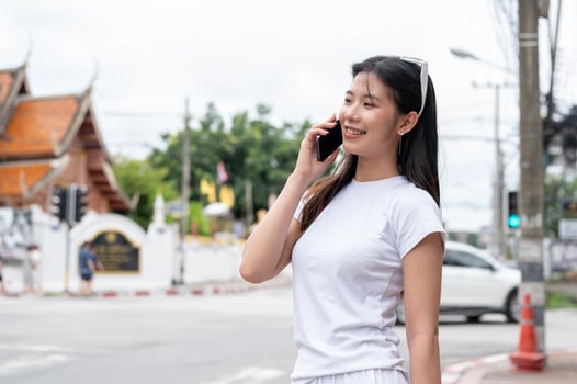 A beautiful Asian woman is talking on the phone while standing by the street in the city. photo
