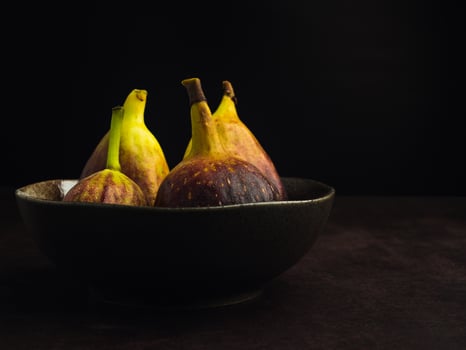 A pile of ripe figs fruit on a bowl with a black background. High Vitamins fruit. Close-up photo. Healthy fruits and healthcare concept photo