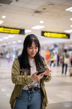 A positive young Asian female traveler is using her smartphone while standing in the airport. photo