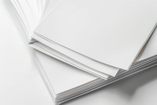 A stack of blank sheets of paper resting on a smooth surface indoors during daylight photo