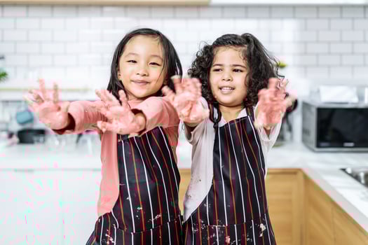 Group of two Diverse Family, Asian and Arab Preschool kid person make Cake cooking in kitchen, little girl shows dirty hands in dough having fun in kitchen, Cream mess over face photo
