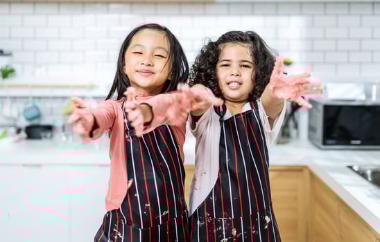 Group of two Diverse Family, Asian and Arab Preschool kid person make Cake cooking in kitchen, little girl shows dirty hands in dough having fun in kitchen, Cream mess over face photo