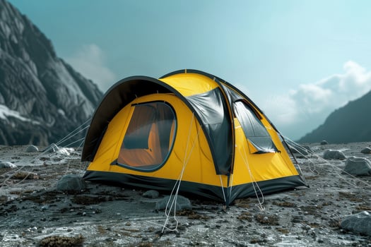 A yellow camping tent set up on rocky terrain in a mountainous area under a bright sky during daytime photo