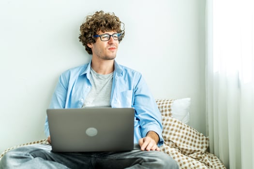 Work from home. Young caucasian man working on computer laptop and looking away, study online listening learning education course conference calling sit laying down on bed, freelancer at home photo