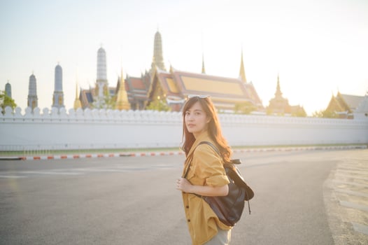 Traveler asian woman in her 30s, backpack slung over her shoulder, explores the intricate details of Wat Pra Kaew with childlike wonder. Sunlight dances on the golden rooftops. photo