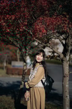 Asian woman in Kyoto's fall, wearing a casual dress, enjoys the beauty of nature, capturing cheerful smiles amid vibrant foliage and the scenic allure of Japan. photo