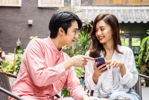 Happy Young asian woman sitting with boyfriend at cafe table, discussing over on smartphone, Young couple looking at mobile phone shopping online and share information together in coffee shop photo