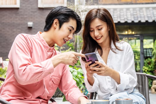 Happy Young asian woman sitting with boyfriend at cafe table, discussing over on smartphone, Young couple looking at mobile phone shopping online and share information together in coffee shop photo