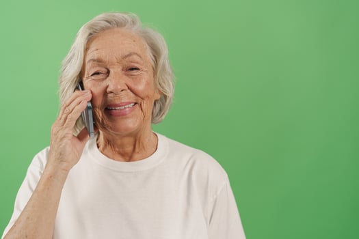 An elderly woman smiles brightly while talking on the phone, with a vibrant green background photo