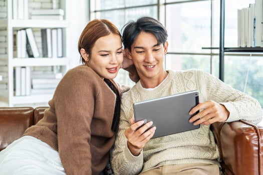 Happy asian young couple looking at digital computer tablet screen, relaxing on comfortable couch. Loving couple shopping online in internet store, watching media content online photo