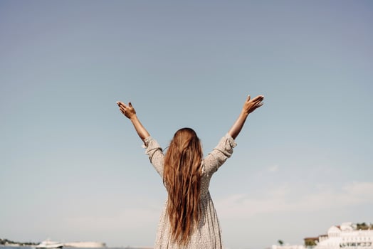A woman with long hair is standing on the beach, looking up at the sky. She is wearing a dress and she is happy. photo