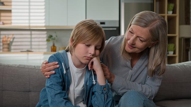 Loving senior mature Caucasian elderly 50s woman granny female touch calming offended stressed bored little kid boy child son grandson sofa grandmother parent ask forgiveness cheering up talk hug home photo