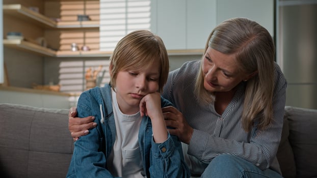 Loving senior mature Caucasian elderly 50s woman granny female touch calming offended stressed bored little kid boy child son grandson sofa grandmother parent ask forgiveness cheering up talk hug home photo
