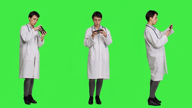 General practitioner playing games on mobile phone app, having fun with online gaming competition against greenscreen backdrop. Cheerful doctor relaxing with internet game. Camera A. photo