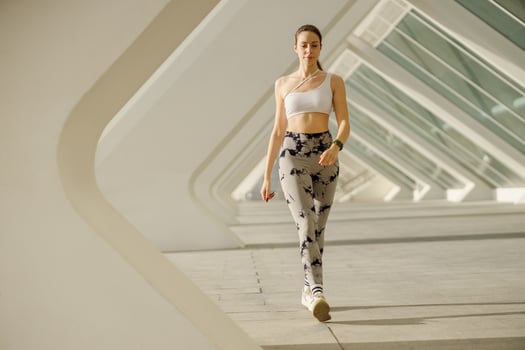 Young woman in sportswear is crossing on modern buildings background. Active lifestyle concept photo