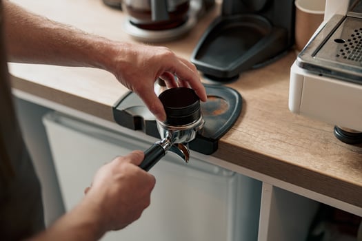 Barista pressing ground coffee into portafilter with tamper photo