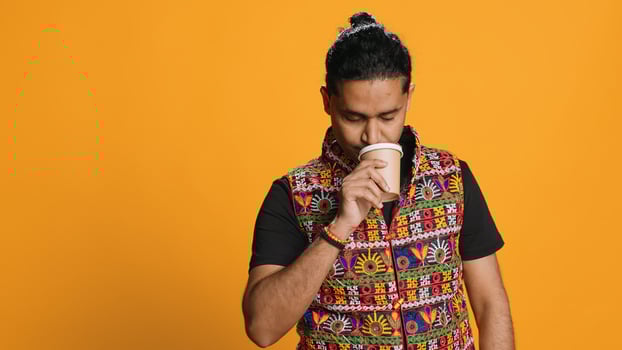 Tired man yawning, sipping fresh coffee from disposable paper cup to wake up and be more energic. Exhausted person drinking caffeinated beverage, isolated over studio background, camera A photo