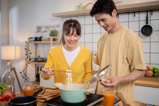 A lovely young Asian couple is enjoying making noodles together in the kitchen. photo
