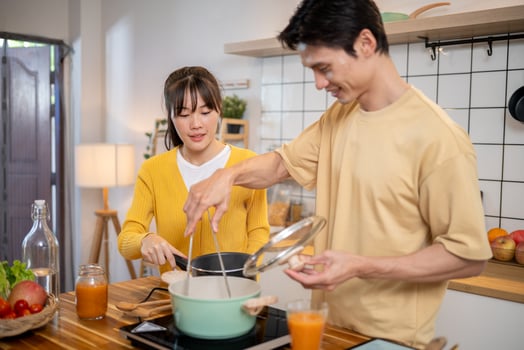A pretty and positive Asian woman is helping her boyfriend in the kitchen as they cook together. photo