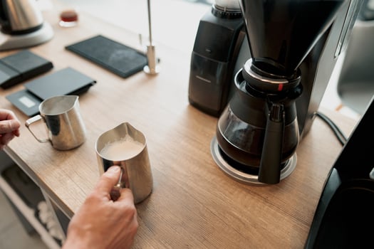 Barista frothed milk for latte in a steel jug photo