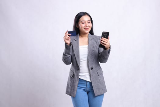 beautiful young woman office smile hold mobile phone smartphone and hold credit debit member card wearing grey suit isolated on white background. for communication, finance, transaction content photo