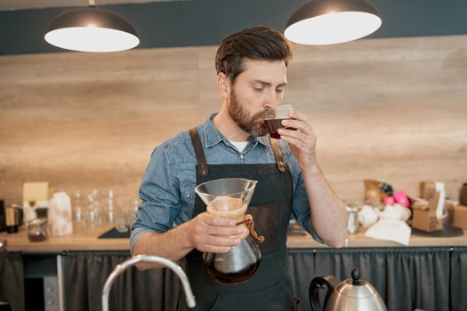 Barista tasting a freshly brewed filter coffee standing behind counter photo