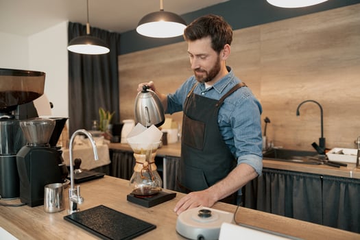 Man barista wearing apron making filter coffee in cafeteria photo