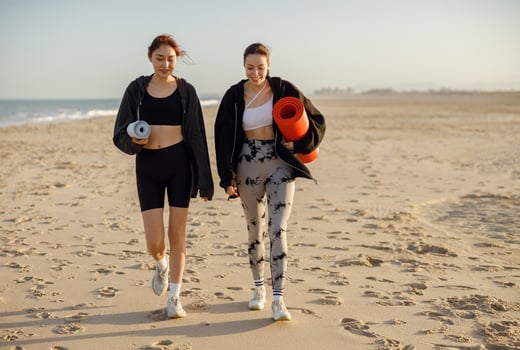 Two young fit women walking on the beach with their yoga mats after doing morning gym photo