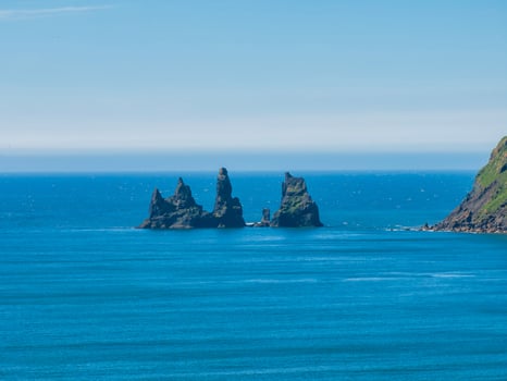 Aerial view of three rocky islands covered in green vegetation, surrounded by calm blue waters and clear skies, showcasing Iceland's dramatic cliffs and rugged coastline. photo