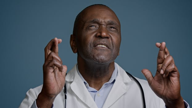 Close-up African American man in studio blue background hopeful male doctor surgeon crosse fingers pray good luck make wish dreaming praying success ask help believe in victory waiting great result photo