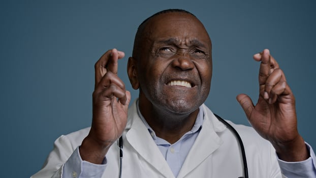 Close-up mature man in studio on gray background hopeful doctor surgeon crosses fingers for good luck makes wish dreaming praying for success asks for help believe in victory waiting for great results photo