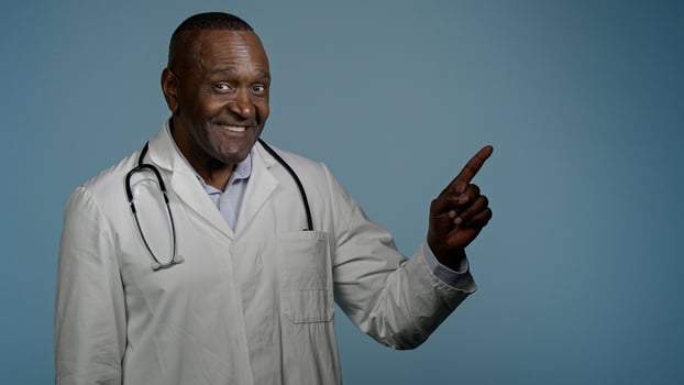 African American man doctor medical worker in white coat male healthcare employee medic customer in studio blue background pointing index finger making choice choosing smiling good selection medicare photo