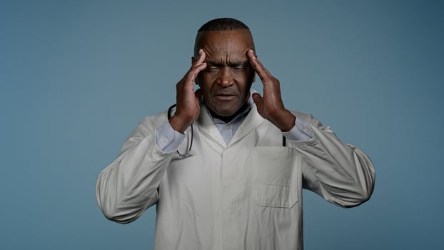 Unhappy African American man doctor male healthcare employee medical worker in blue studio feeling headache exhaustion suffering from chronic migraine pain in head illness pressure massage temples photo