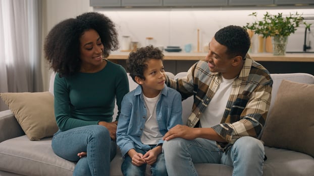 African American happy family portrait couple man father male dad mom woman mother female sitting indoor couch talking speak cuddle stroking head little boy child son kid parent tenderness living room photo