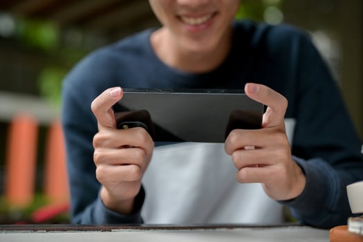 A cropped image of a joyful young Asian man happily playing a mobile game on his smartphone. photo