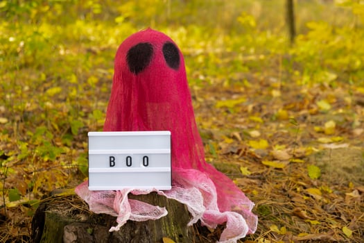 Lightbox BOO text Creative handmade Halloween holiday decoration. pink ghost in autumn leaves forest. Zero waste homemade decor. Mystic place supernatural photo