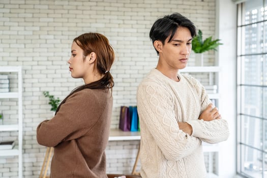 Photo of resentful asian guy and girl acting like arguing couple and not speaking to each other, while standing together in living room at home