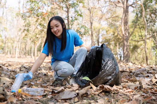 Woman Picking Litter with Bag in Leafy Forest photo