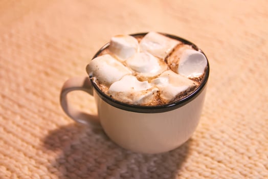 Hot fresh cocoa drink in a ceramic mug with melting sweet marshmallows on cozy knitted background photo