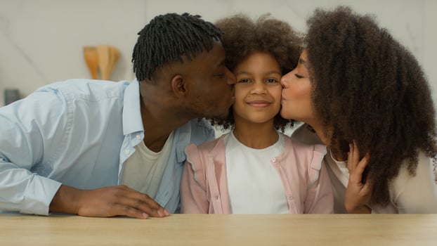 African American family portrait smiling love affectionate bonding relationship biracial happy together in kitchen home mother father with daughter kissing parents kiss little girl kid child to cheeks photo