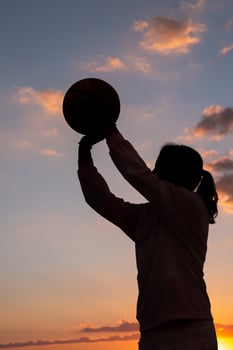 silhouette of a teenage girl holding a basketball ball in her hands at sundown photo