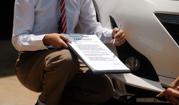 Side view of writing on clipboard while insurance agent examining car after accident photo