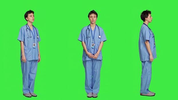 Young nurse with medical expertise poses with confidence, wears blue scrubs uniform and smiling against greenscreen backdrop. Health assistant gives support to doctors as profession. Camera A. photo