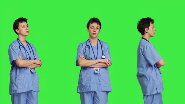 Portrait of confident medical assistant posing with arms crossed in studio, standing against greenscreen backdrop. Successful nurse with healthcare expertise wearing blue scrubs uniform. Camera B. photo